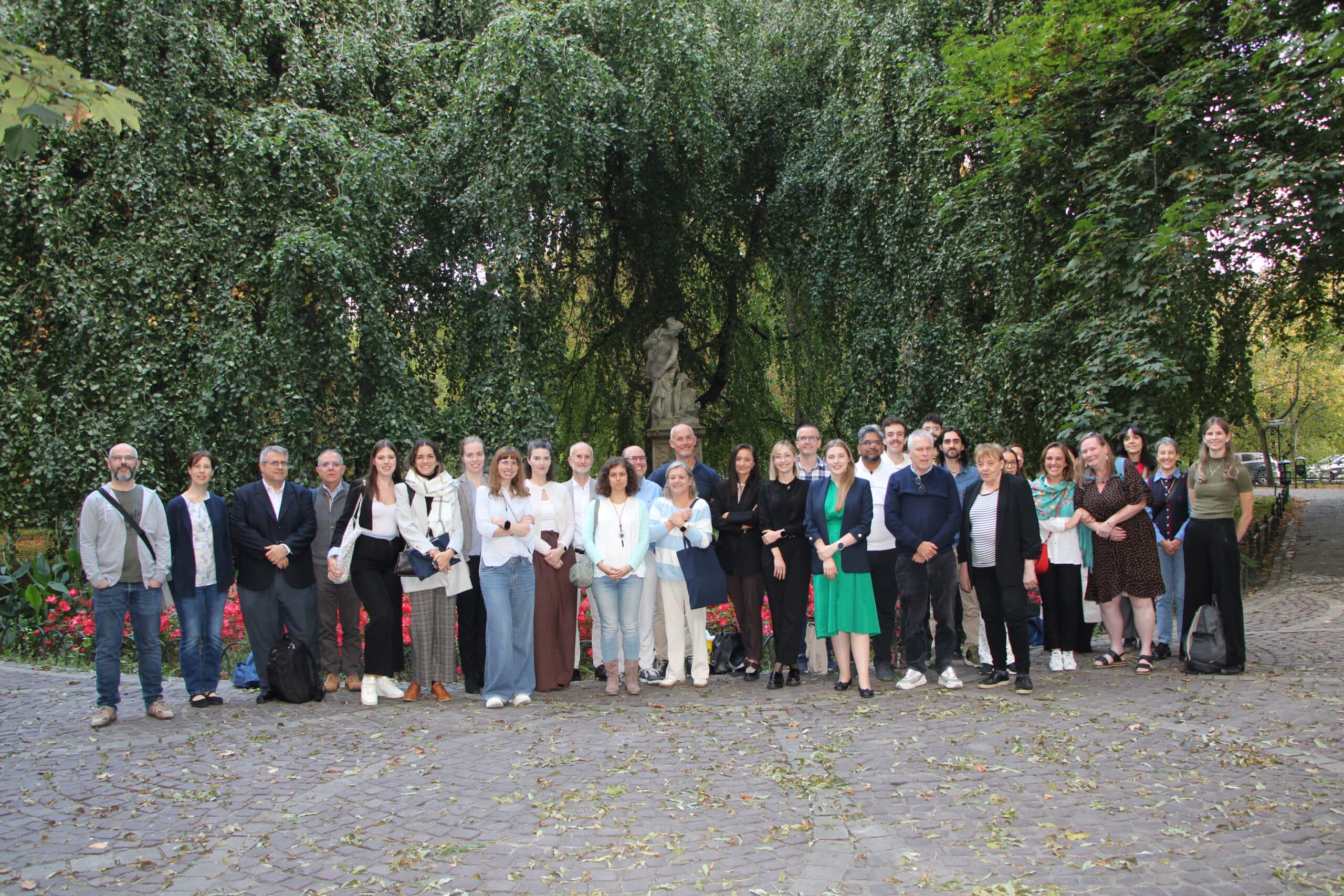 Members of the ForMAT consortium standing together outdoors in Kraków, in front of a large weeping tree and a stone statue.